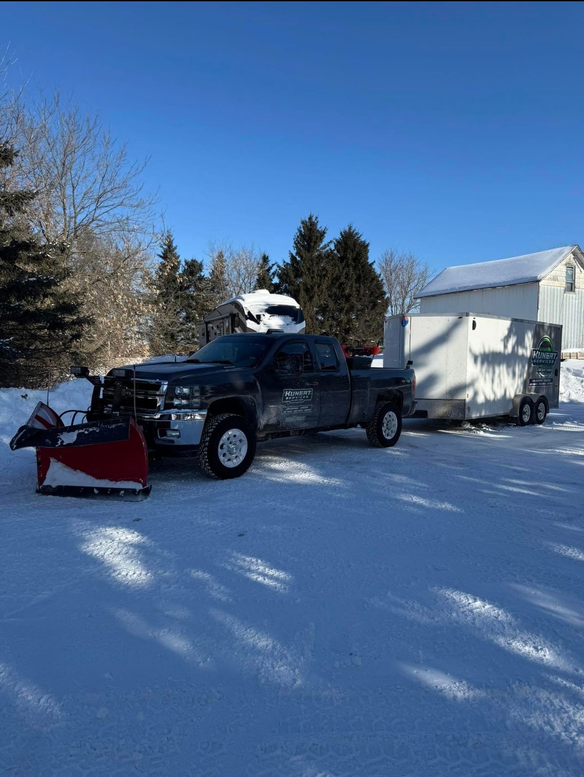 Truck with v-shaped snowplow on front and company trailer behind